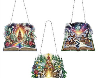 May include: Three Christmas-themed ornaments shaped like open books with a 3D effect. Each ornament features a different winter scene: a snowy forest with a Christmas tree, a village with snow-covered houses, and a forest with a Christmas tree and a glowing light.
