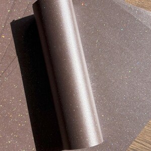 May include: A roll of shimmering, bronze-coloured paper with a subtle glitter effect. Several sheets of the same paper are visible in the background, creating a textured surface.