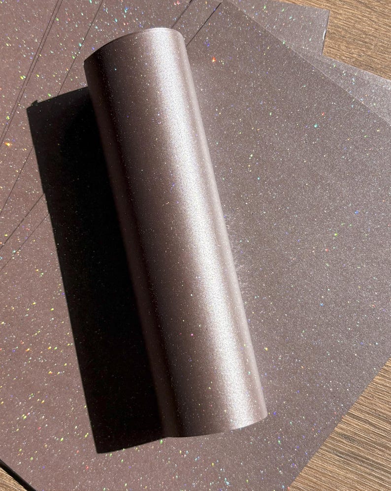 May include: A roll of shimmering, bronze-coloured paper with a subtle glitter effect. Several sheets of the same paper are visible in the background, creating a textured surface.