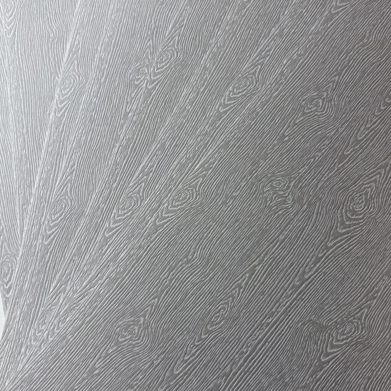 May include: Close-up of a gray wood-grain pattern. The design features diagonal lines with knots, creating a textured surface. The color is a neutral gray, suitable for various design applications.