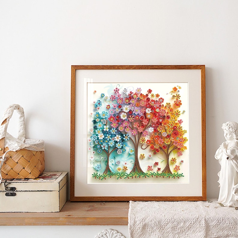May include: A framed artwork featuring four stylized trees with colorful paper quilling flowers. The trees transition from blue to pink to red to orange, with green grass at the base. The frame is a warm brown color.