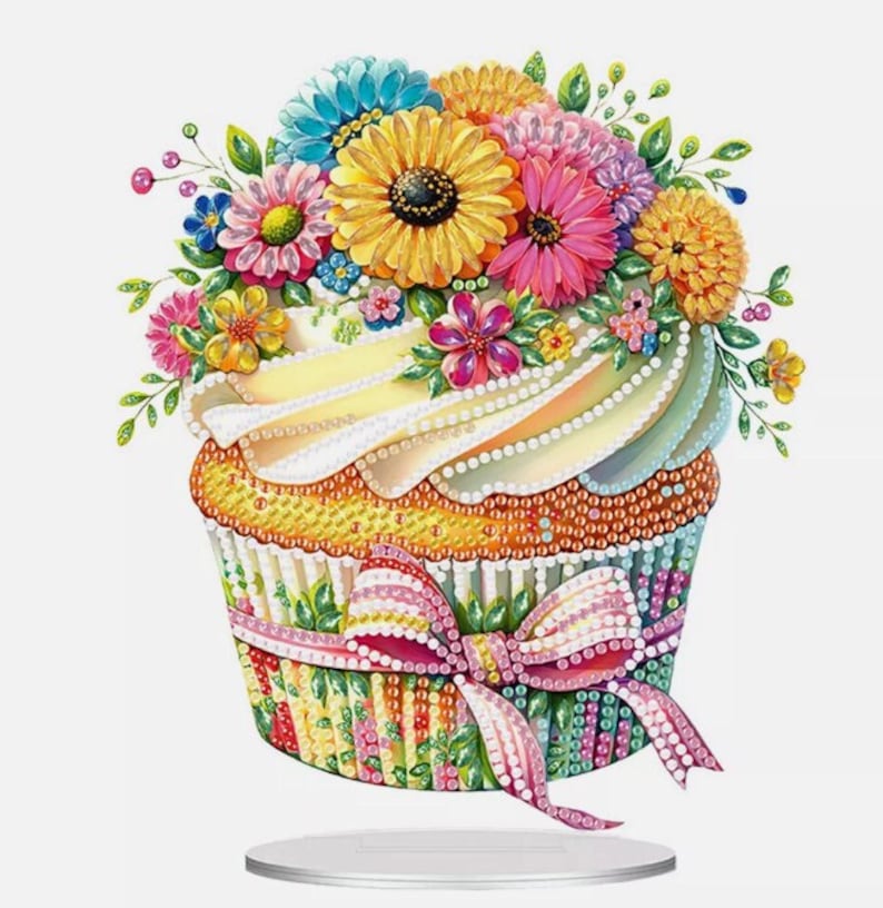 May include: A colorful cupcake with a white frosting and a bouquet of flowers on top. The cupcake is decorated with a pink and white striped ribbon and a bow.