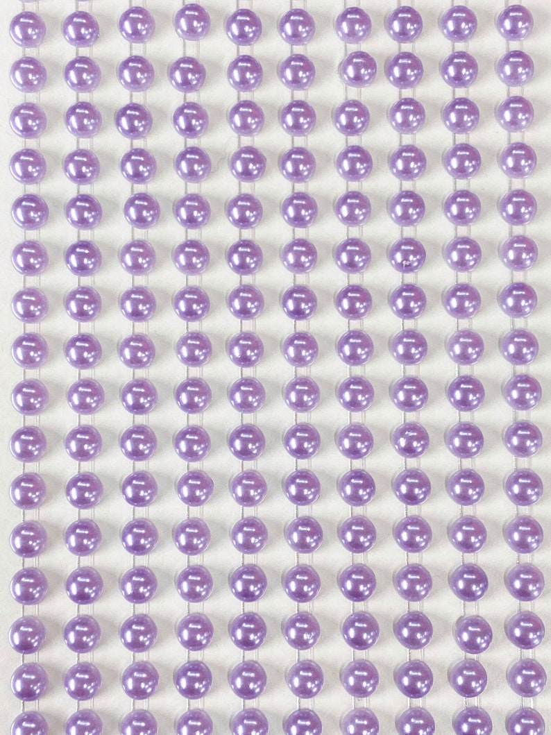 May include: A sheet of self-adhesive purple pearl embellishments. The pearls are arranged in rows on a white sheet.