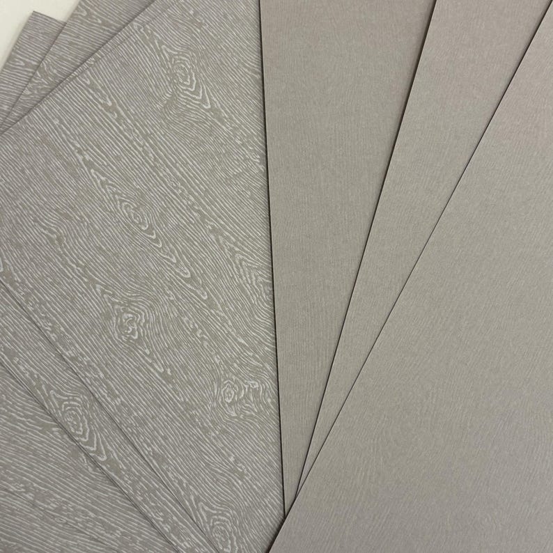 May include: A collection of gray rectangular sheets, some with a wood grain pattern and others with a smooth, solid color. The sheets are fanned out, showcasing the different textures and designs.