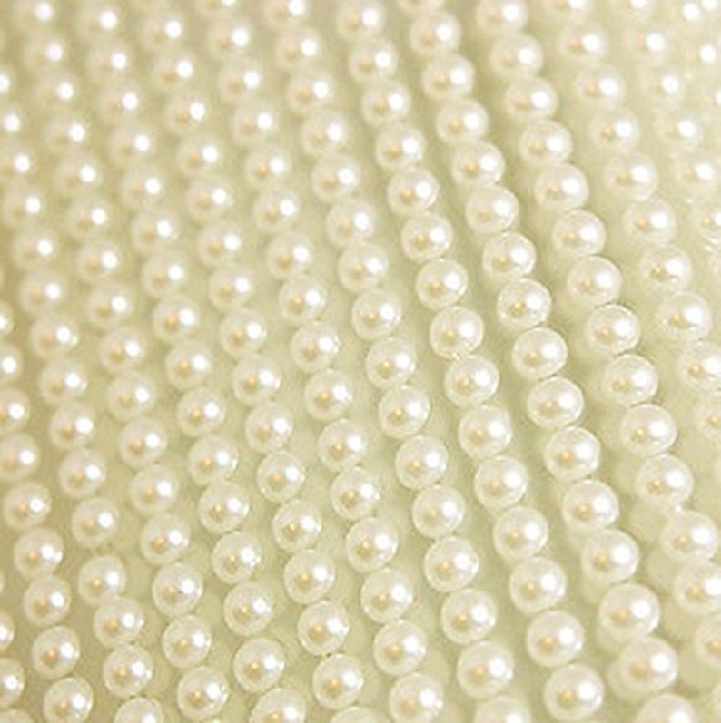 May include: A close-up of a strand of white pearl beads. The beads are small and round, and they are arranged in a straight line.