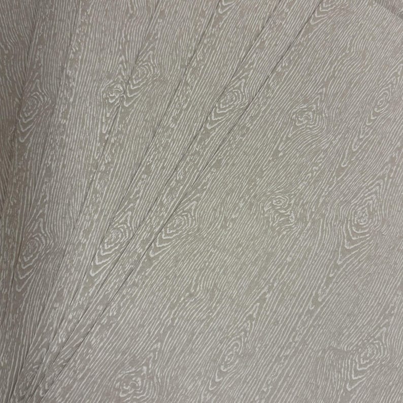 May include: A stack of light gray paper sheets with a wood grain pattern. The design features detailed white lines mimicking the texture of wood, including knots and grain patterns. The sheets are fanned out, showcasing the repeating design.