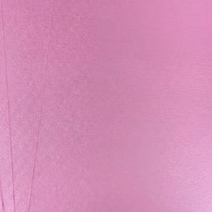 The image is a close-up of a pink surface, possibly a piece of paper or fabric.