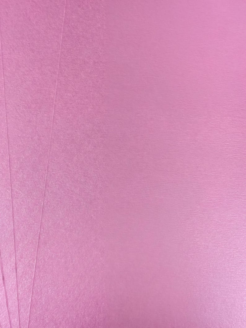 The image is a close-up of a pink surface, possibly a piece of paper or fabric.