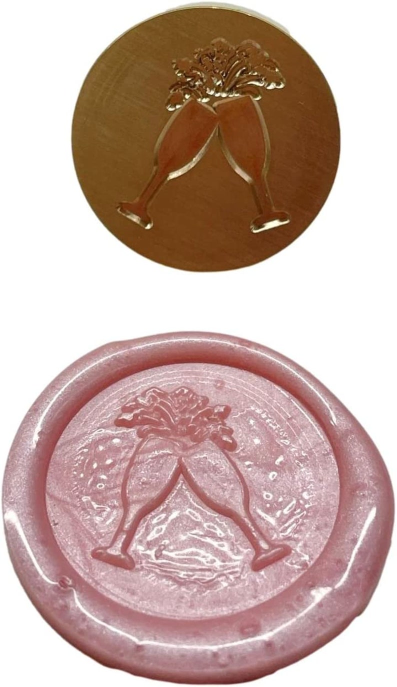 May include: A pink wax seal with a design of two champagne glasses clinking together. The glasses are filled with a bubbly liquid and there are stars around them.