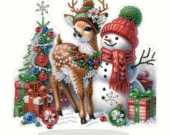 May include: A 3D diamond painting kit featuring a snowman and a deer standing next to a Christmas tree with presents and ornaments. The kit includes a clear acrylic base and a stand.