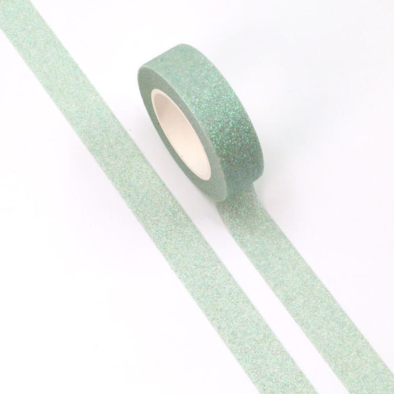 May include: A roll of light green glitter washi tape with a white core. The tape is unrolled on a white surface.