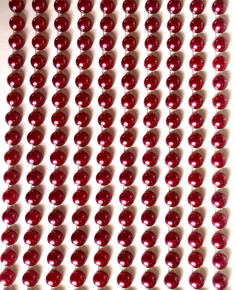 May include: A sheet of burgundy pearl embellishments, arranged in rows on a white background. The pearls are small and round, with a glossy finish.