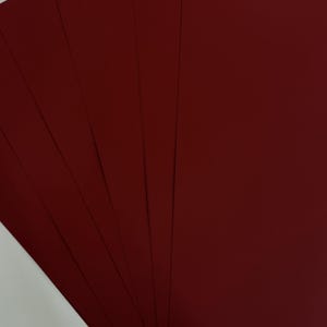 May include: A stack of burgundy-colored cardstock paper fanned out, showcasing the rich, deep red hue. The paper has a smooth, matte finish, and the edges are neatly aligned. The image highlights the color and texture of the paper.