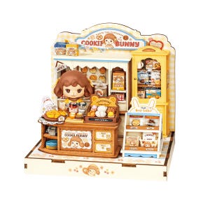 May include: A miniature wooden cookie shop playset featuring a brown-haired character figure, a yellow display cabinet, and a counter with various cookie accessories. The signage displays the text COOKIE BUNNY, TASTE THE CUTENESS, and HANDMADE.