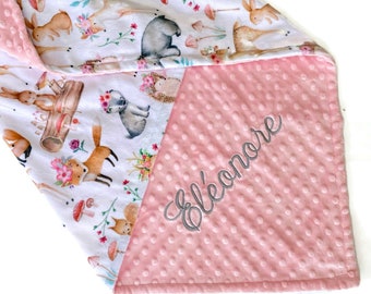 Op de afbeelding: Een roze en witte babydeken met een print van bosdieren aan de ene kant en een roze minky stof aan de andere kant. De minky stof heeft de naam "Eleanor" geborduurd in grijze draad.