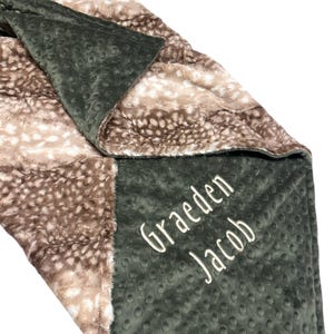 May include: A green and brown baby blanket with a fawn print on one side and a soft, textured fabric on the other. The blanket is personalized with the names "Graeden Jacob" embroidered in white.