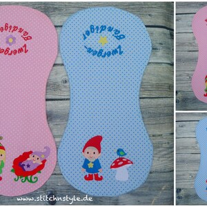 Puede incluir: Art&iacute;culos de tela rosa y azul con lunares y dise&ntilde;os de gnomos bordados. El art&iacute;culo rosa tiene un gnomo y un beb&eacute; durmiendo en un trineo rojo. El art&iacute;culo azul tiene un gnomo, una seta y un p&aacute;jaro. Texto en alem&aacute;n bordado en la parte superior.