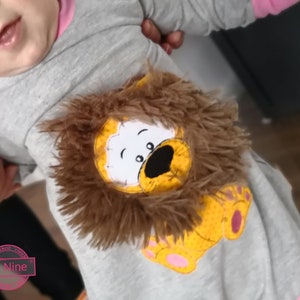 May include: A gray long-sleeved onesie with a pink trim. The onesie features an embroidered lion with a brown furry mane. The lion is wearing a yellow and orange body with pink paw prints.