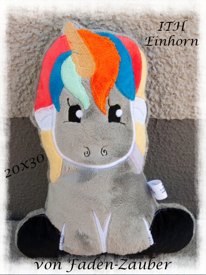 May include: A plush unicorn toy with a gray body, black hooves, and a colorful mane and tail. The mane features red, orange, blue, and green hues. The text "ITH Einhorn" and "20x30" are visible. The text "von Faden-Zauber" is also present.
