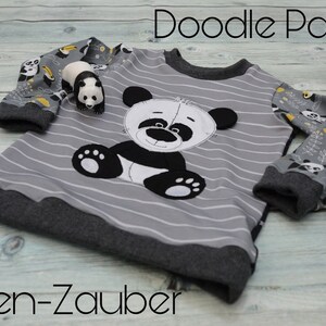 May include: A gray and black striped long-sleeved shirt with a black and white panda applique. The sleeves have a gray and white panda print with yellow accents. The shirt has the text "Doodle Panda" and "Faden-Zauber" printed on it.