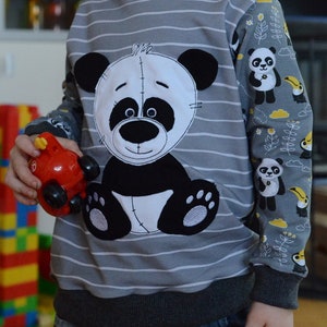 May include: A gray and white striped sweatshirt with a black and white panda bear applique. The sleeves have a panda and toucan print on a gray background.