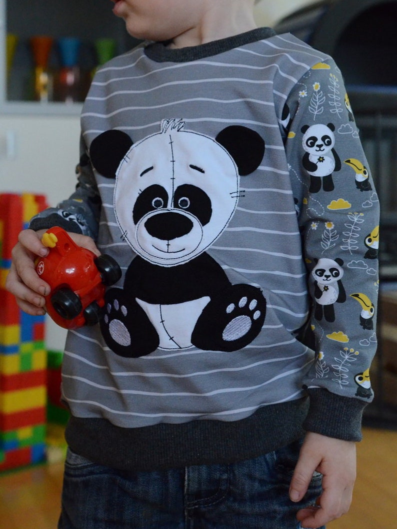 May include: A gray and white striped sweatshirt with a black and white panda bear applique. The sleeves have a panda and toucan print on a gray background.