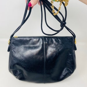 May include: A black leather crossbody bag with a gold zipper and a long adjustable strap.