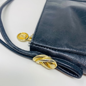 May include: Black leather handbag with a gold-tone clasp and a gold-tone logo. The bag has a long strap.