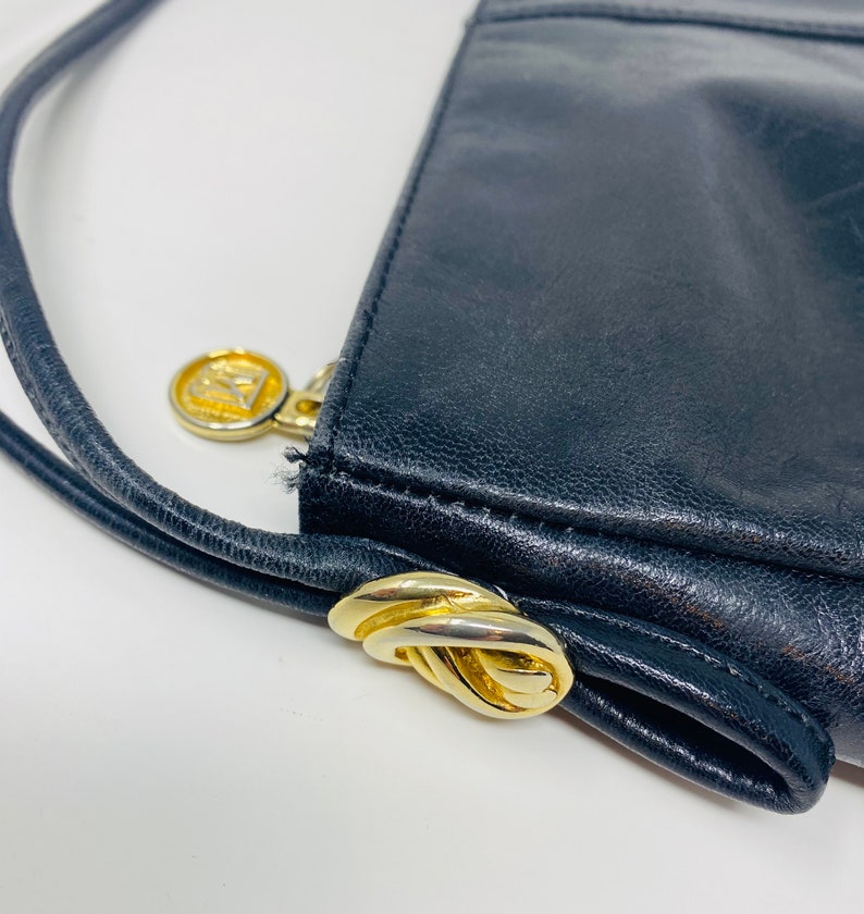 May include: Black leather handbag with a gold-tone clasp and a gold-tone logo. The bag has a long strap.