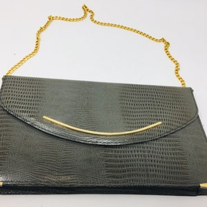 May include: A grey snakeskin clutch bag with a gold chain strap and a gold metal bar closure.