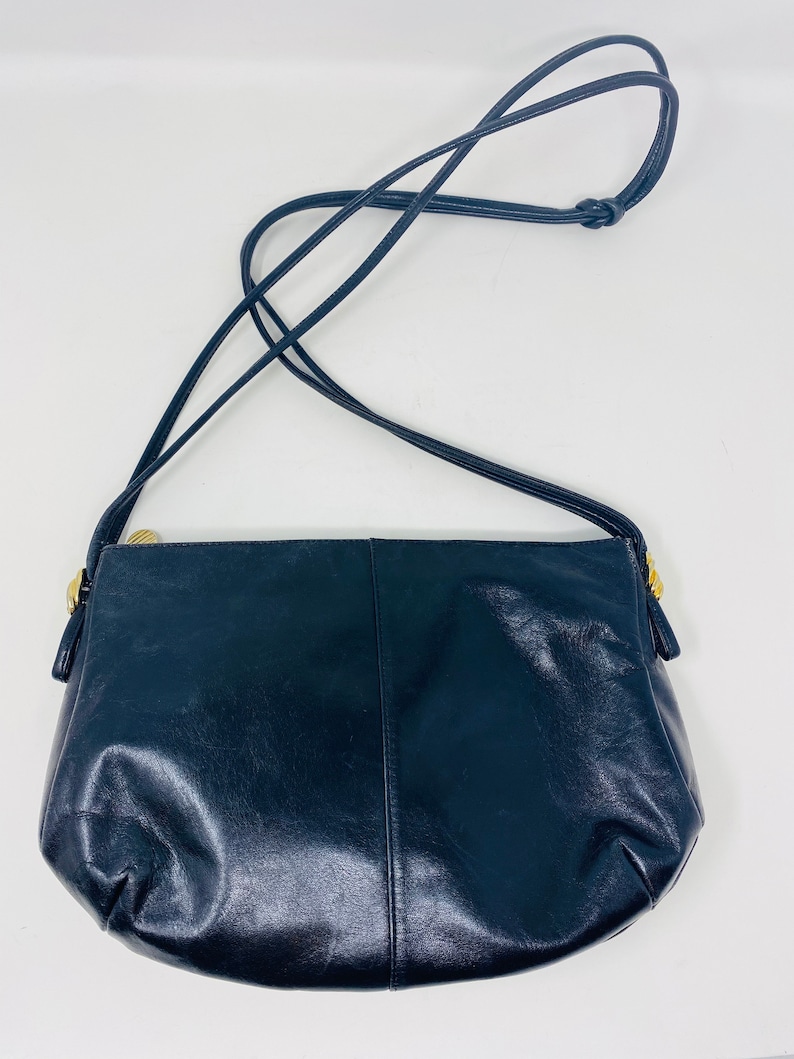 May include: A black leather shoulder bag with a gold zipper and a long strap.