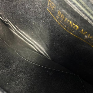 May include: The inside of a black leather purse with a gold embossed label that reads "Bruno Magli Italy".