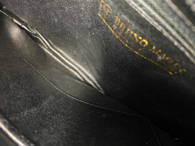 May include: The inside of a black leather purse with a gold embossed label that reads "Bruno Magli Italy".