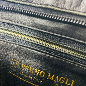 May include: Close-up of a black leather interior with a gold zipper and a gold label that reads "BRUNO MAGLI Made in Italy Bologna".