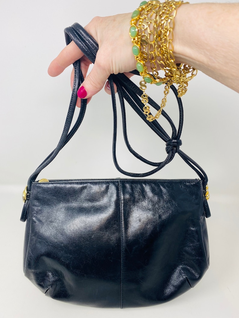 May include: A black leather crossbody bag with a gold zipper and a long adjustable strap.