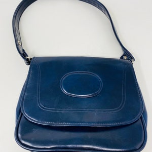 May include: A dark blue leather shoulder bag with a circular design on the front flap.