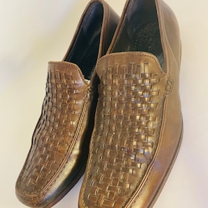 May include: A pair of brown leather loafers with a woven pattern on the vamp. The shoes have a square toe and a low heel. The leather has a slight sheen. The shoes appear to be unworn.