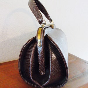 May include: A brown faux leather handbag with a top handle and a gold clasp. The bag has a textured, snake-like pattern.