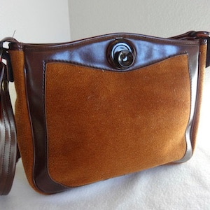 May include: A brown suede shoulder bag with a brown leather flap and a single button closure. The bag has a long brown leather strap.