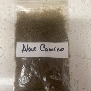 May include: A small clear plastic bag filled with a brown powder labeled "Ashe Camino".