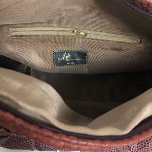 May include: The inside of a brown leather purse with a zippered pocket and a label that reads "Arto Leather Products, New York".
