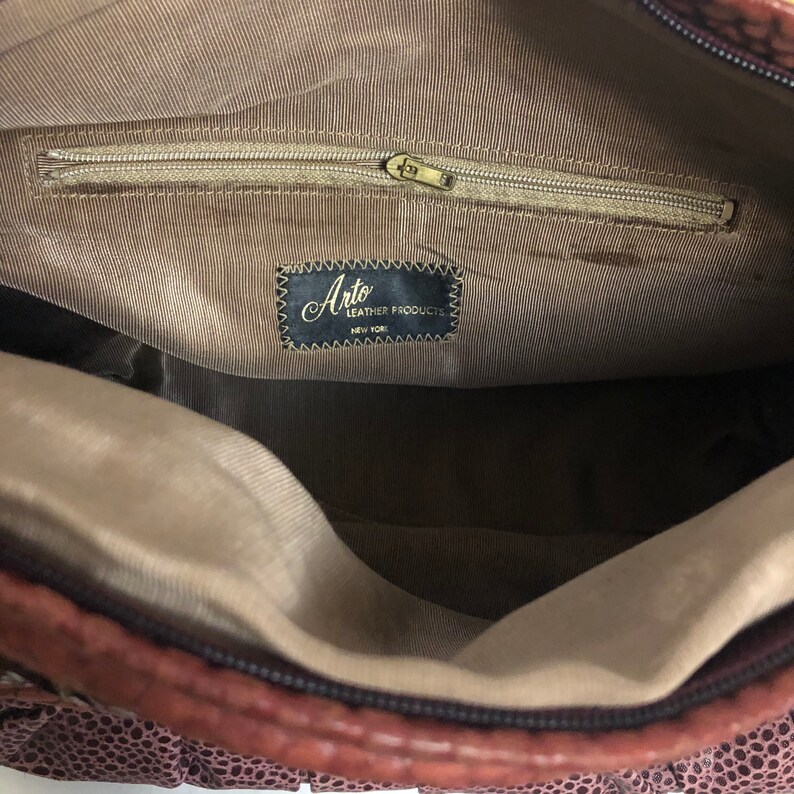 May include: The inside of a brown leather purse with a zippered pocket and a label that reads "Arto Leather Products, New York".