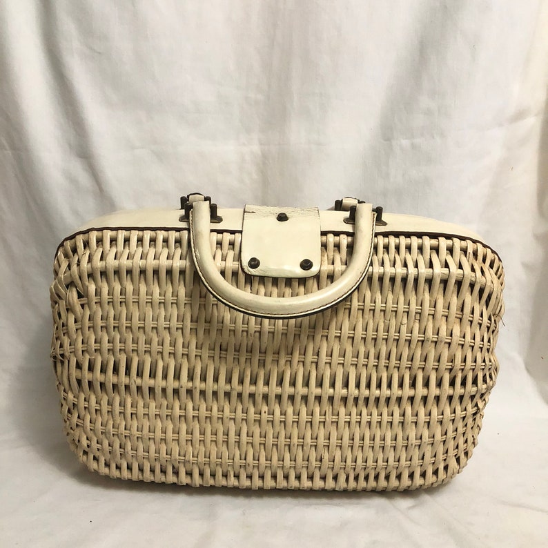 Puede incluir: Un bolso de mimbre blanco con asa de cuero blanco y solapa de cuero blanco con cierre de metal.
