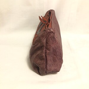 May include: A brown leather clutch purse with a textured surface and a brown leather strap. The purse has a silver metal accent on the front.