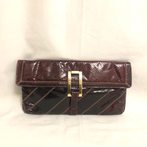 May include: A burgundy snakeskin clutch with a gold clasp and a geometric pattern.