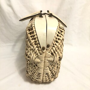 Puede incluir: Un bolso de mimbre blanco con un marco de metal blanco y un dise&ntilde;o tejido. El bolso tiene dos asas y un cierre de broche.