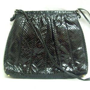 May include: A black snakeskin handbag with a long strap. The bag has a textured surface and a flap closure.