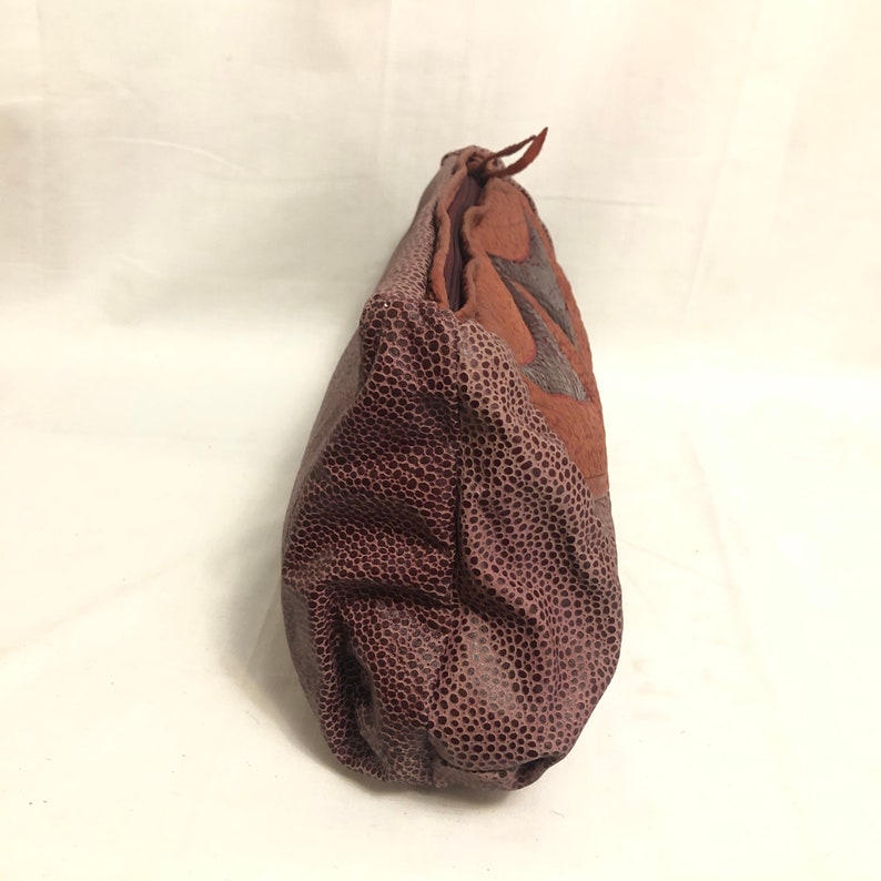 May include: A brown leather pouch with a textured surface. The pouch has a zipper closure and a brown leather strap.