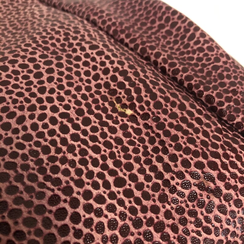 May include: Close-up of a dark purple textured fabric with a small white mark.