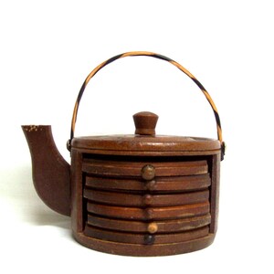 May include: Wooden teapot-shaped coaster holder with a brown finish and a black and orange striped handle. The holder has six round coasters stacked inside.
